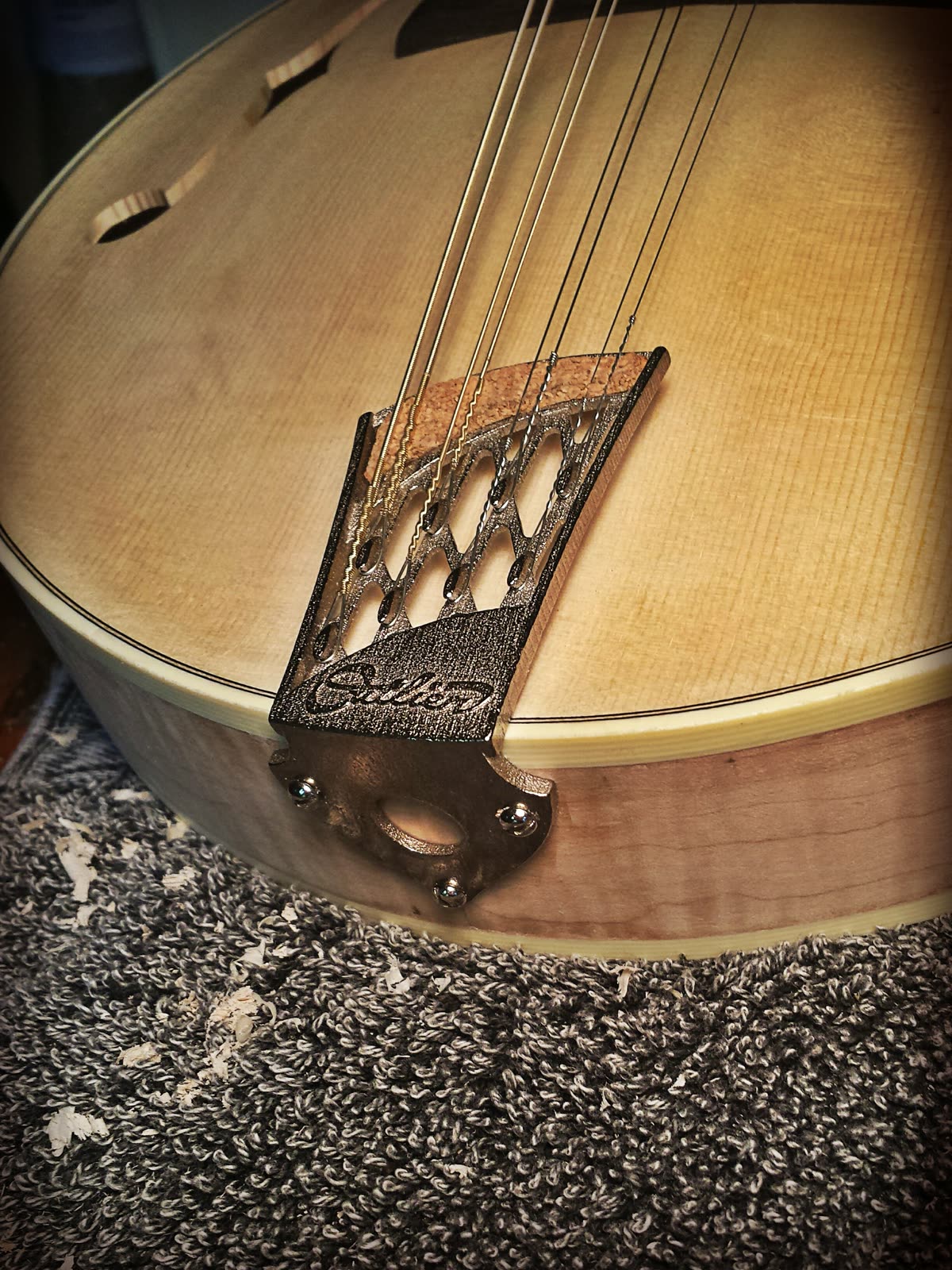 Cast tailpiece — cutwork, nickel-plated stainless/bronze, mounted on a mandolin body in the white